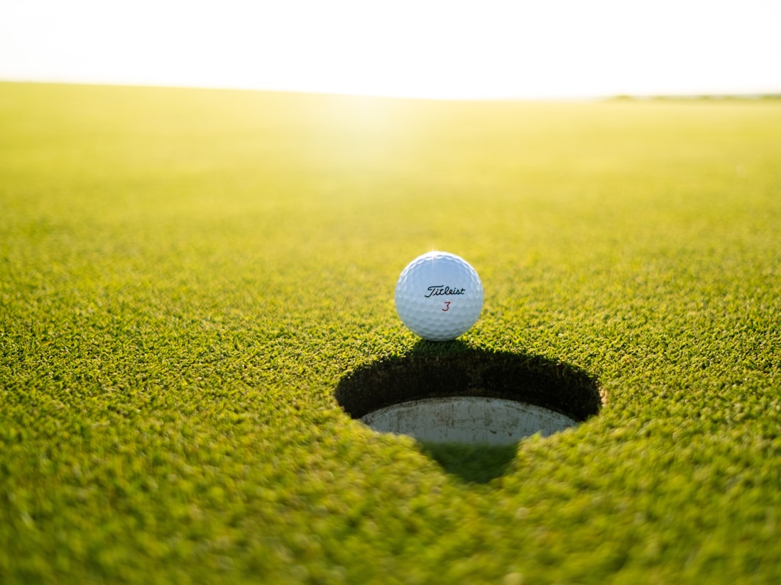 A golf ball resting on the lip of the hole on a sunlit putting green